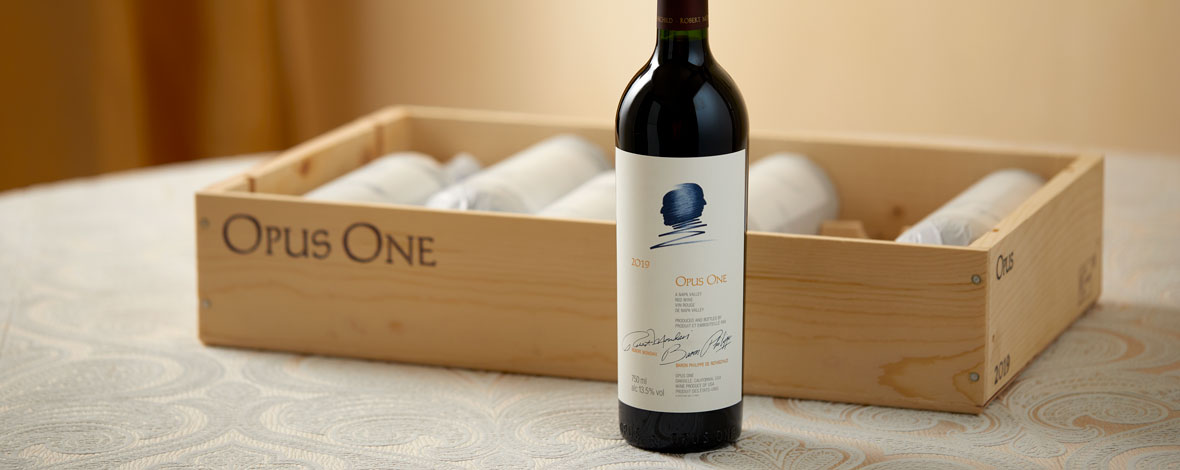 A bottle of Opus One 2019 next to a wooden case of six bottles